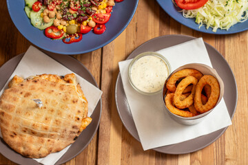 Onion rings with white sauce on light plate on wooden table with side dishes in the backgorund.