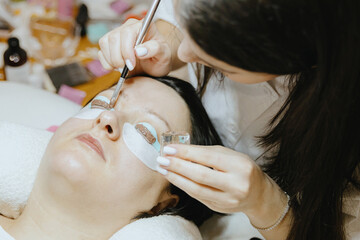 Girl cosmetologist laminates and paints woman eyelashes