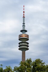 Naklejka premium The tall concrete tower rises proudly, surrounded by lush green trees, under a clear blue sky with fluffy white clouds. Its observation deck offers stunning views of the scenic landscape below.
