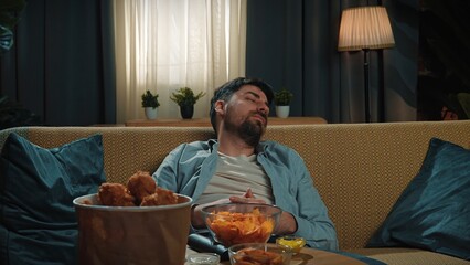 Bearded man spending time at home with fast food delivery, sits on couch and watching tv, getting...