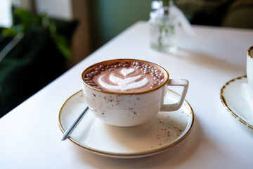Steaming cup of hot chocolate decorated with latte art and chocolate sprinkles sits on a table in a cozy cafe, creating a warm and inviting atmosphere