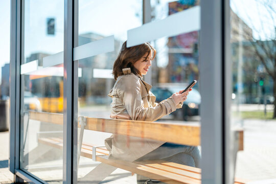 Young woman using mobile phone at a bus stop in the city
