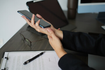 An asian tired business woman working for a long time and typing the computer, and using the mobile phone, so her wrist is hurt and she is massaging her hurt wrist by another hand, an office syndrome.