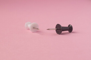 Black and white push pins on pink paper background top view