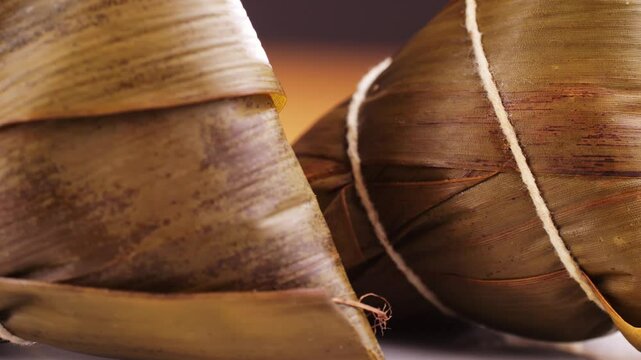 Hand holding zongzi (rice dumpling) with savoury fillings wrapped in bamboo or reed leaves.