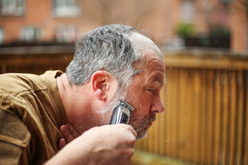 Self-care moment: older man shaving his beard outside, hair flying in the air