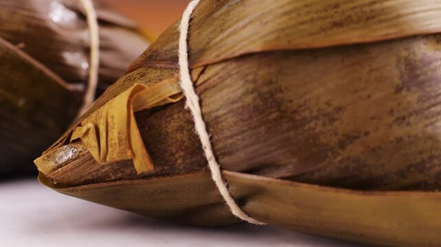 Hand holding zongzi (rice dumpling) with savoury fillings wrapped in bamboo or reed leaves.