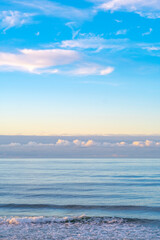 View of an empty sea with a blue sky partially covered by clouds. Several layers of clouds above the water.