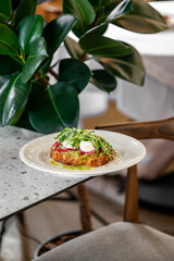 A beautifully presented plate of gourmet toast topped with fresh greens and radishes, set on a stylish table with a leafy plant in the background.