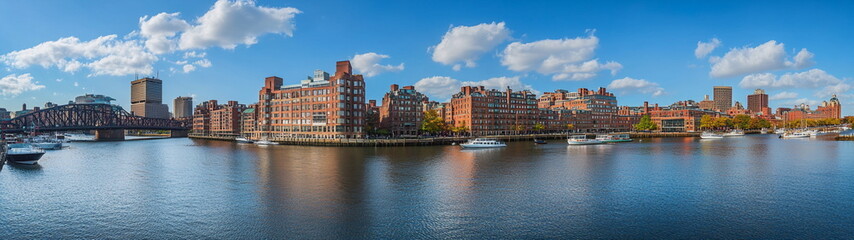 Fototapeta premium Traditional city buildings with red brick facades reflecting in the river water under a sunny blue sky. A warm and welcoming urban setting for stock and editorial use. 