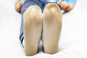 Child feet in dirty stained white socks.Kid soiled contaminated socks while playing outdoors,on unwashed floor.Children clothes bleaching and washing troubles concept