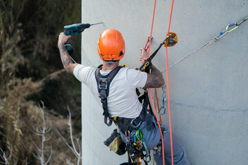 Rope access technician using rotary hammer drill on concrete chimney