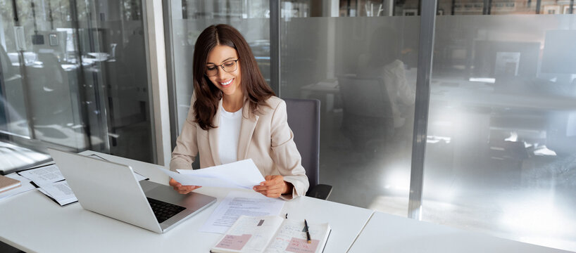 Latin business woman saleswoman working on laptop computer reading financial bank document in office workplace. Young manager businesswoman specialist doing paperwork using pc. Banner, copy space