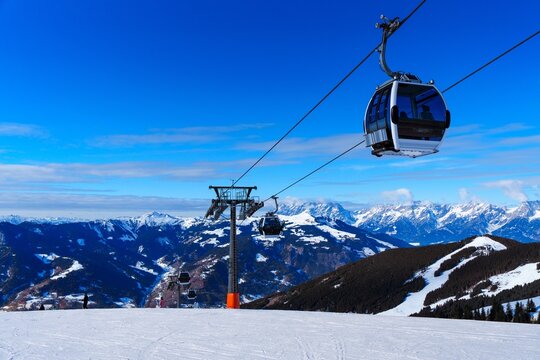 A ski lift traverses a snowy mountainside, providing stunning views of the surrounding snow-capped peaks. The sky is crystal clear, with sparse white clouds dotting the deep blue expanse.