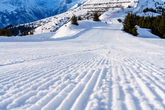 A beautiful winter landscape of a ski slope with freshly groomed snow and mountain peaks in the distance. Perfect for skiing, snowboarding, and other winter sports.