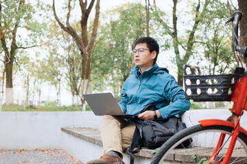 An Asian man using laptop outside