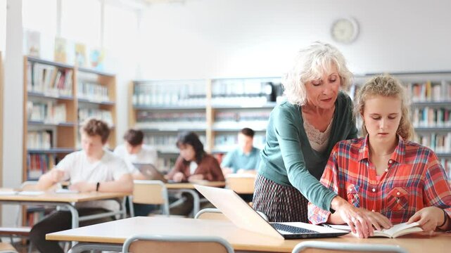 Mature female teacher working with schoolchildren in the library cheks the assignment from a European fifteen-old-year schoolgirl. . High quality 4k footage
