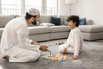 Arabic man playing colorful blocks with little son. Middle Eastern family dressed in traditional...