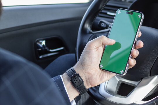 Businessman holding smartphone with green screen in one hand with space for design on steering wheel. driver looking the way to follow. road work business trip. use of technology