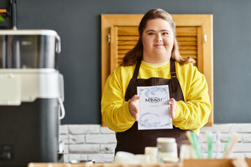 Young woman confidently presenting menu in a cozy cafe setting with a warm atmosphere