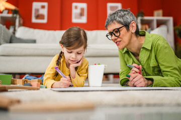 grandma and grandchild play on the floor draw and paint with pen