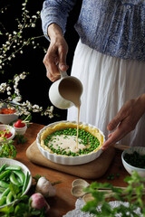 A woman making a vegetarian quich, pouring bottom the egg-cream mixture, close-up. Easter food concept