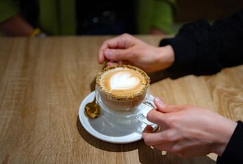 Woman holding pistachio latte with heart shaped foam art in cafe