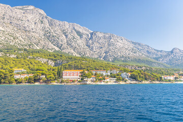 Fototapeta premium Sea coast of the Peljesac Peninsula in Croatia, Europe. Coastal view featuring mountains meeting the sea, green trees and buildings dotting the landscape on a clear, sunny day. Water is blue.