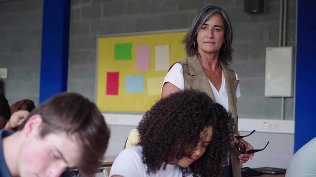 High school students concentrated during exam with teacher watching them, walking around.