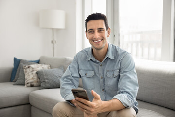 Portrait of smiling Hispanic guy spend free time on internet, chatting or using new mobile amusing...