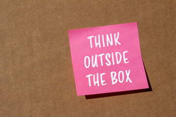 Think outside the box message written on pink paper on brown background. Conceptual think outside the box symbol. Copy space.
