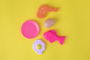 Colorful plastic toy food items, including a fish, chicken leg, egg, plate, and donut, arranged on...