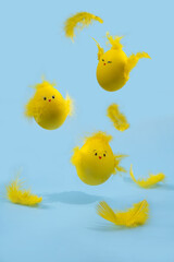 Cute yellow Easter eggs in the shape of chicks surrounded by feathers on a bright blue background. Easter greeating card.