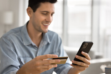 Close up of young man holding credit card and smartphone, smile, completing successful transaction, accessing on-line services, doing online payments, enjoy electronic shopping using digital banking