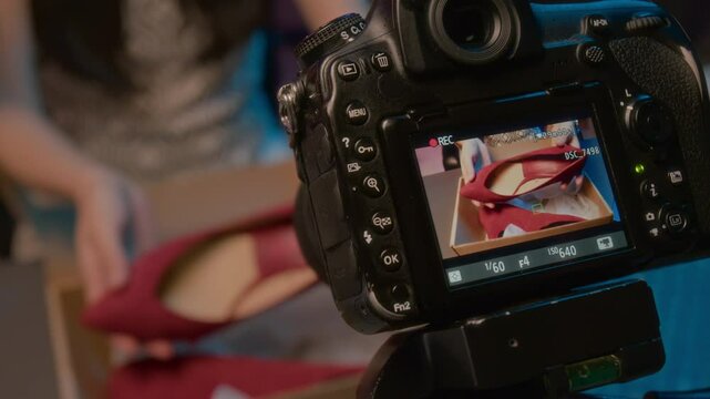 Close-up top view of screen of professional video camera filming hands of unrecognizable woman holding pair of red leather heeled shoes while working at influencer farm