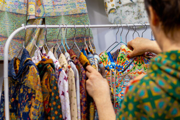 Woman looks at brightly colored folk clothing on rack in store, choosing from variety of colorful...