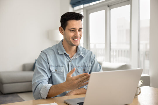 Handsome Latin man sit at table with laptop, enjoy virtual meeting with family or friend, lead personal conversation, or pass job interview remotely. Videocall application usage, digital communication