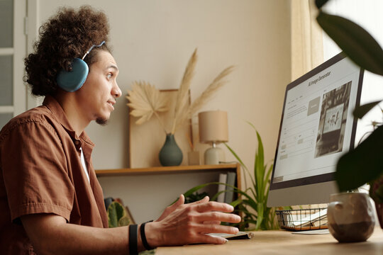Young biracial man looking at picture generated with artificial intelligence on his desktop computer, side view shot