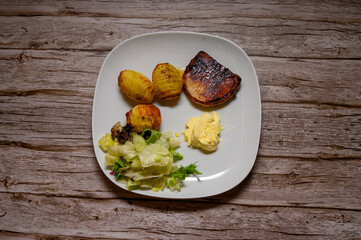A perfectly grilled pork chop is plated alongside golden baked potatoes and a fresh green salad, offering a delightful dinner choice. The meal is arranged on a simple white plate