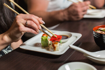 A person dipping sushi into soy sauce with chopsticks