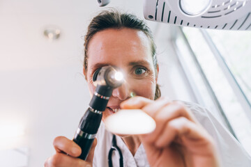 Female doctor performing medical examination using otoscope and tongue depressor