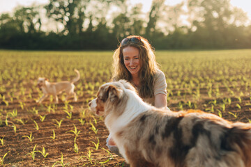 Female farmer smiling and kneeling next to her australian shepherd dog in corn field