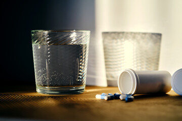 A glass of water and a bottle of pills in the sunlight.