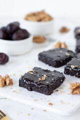 Chocolate brownie with dates and walnuts on white plate in the kitchen. Healthy vegan raw dessert food.