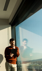 Professional man engages in deep thought while using a tablet next to a large window with city view