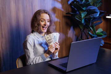 Excited woman holding cash, celebrating online success, winning money, financial achievement, remote work earnings, joyful reaction at laptop
