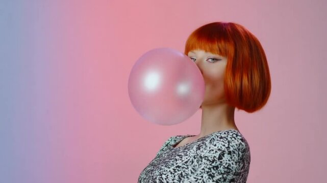 Retro portrait of a woman with bright red hair blowing a large pink bubble gum bubble in front of a colorful pink and blue background.