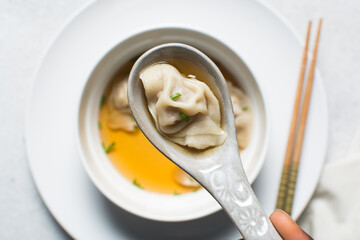 Overhead view of wonton in a ceramic spoon, clear soup with dumplings in a ceramic spoon