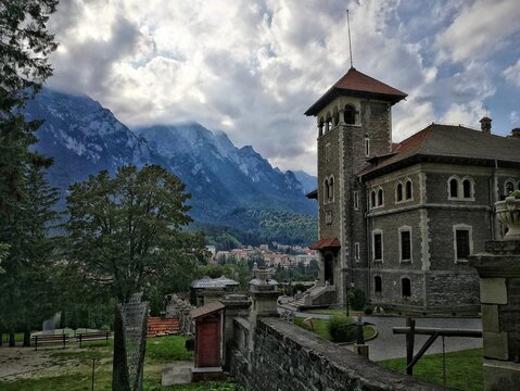 Cantacuzino Castle in Busteni, Romania. Stone castle with arched windows and red-tiled roof, nestled amid lush greenery. 