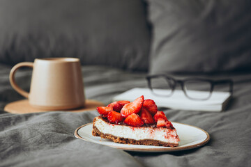 Homemade cheesecake with fresh strawberries and coffee cup on grey bed linen.
